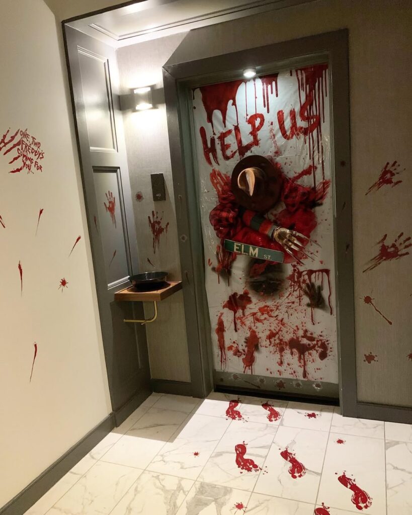 Horror-inspired hallway door display with bloody handprints, "HELP US" message, Freddy Krueger figure, and Elm Street sign.