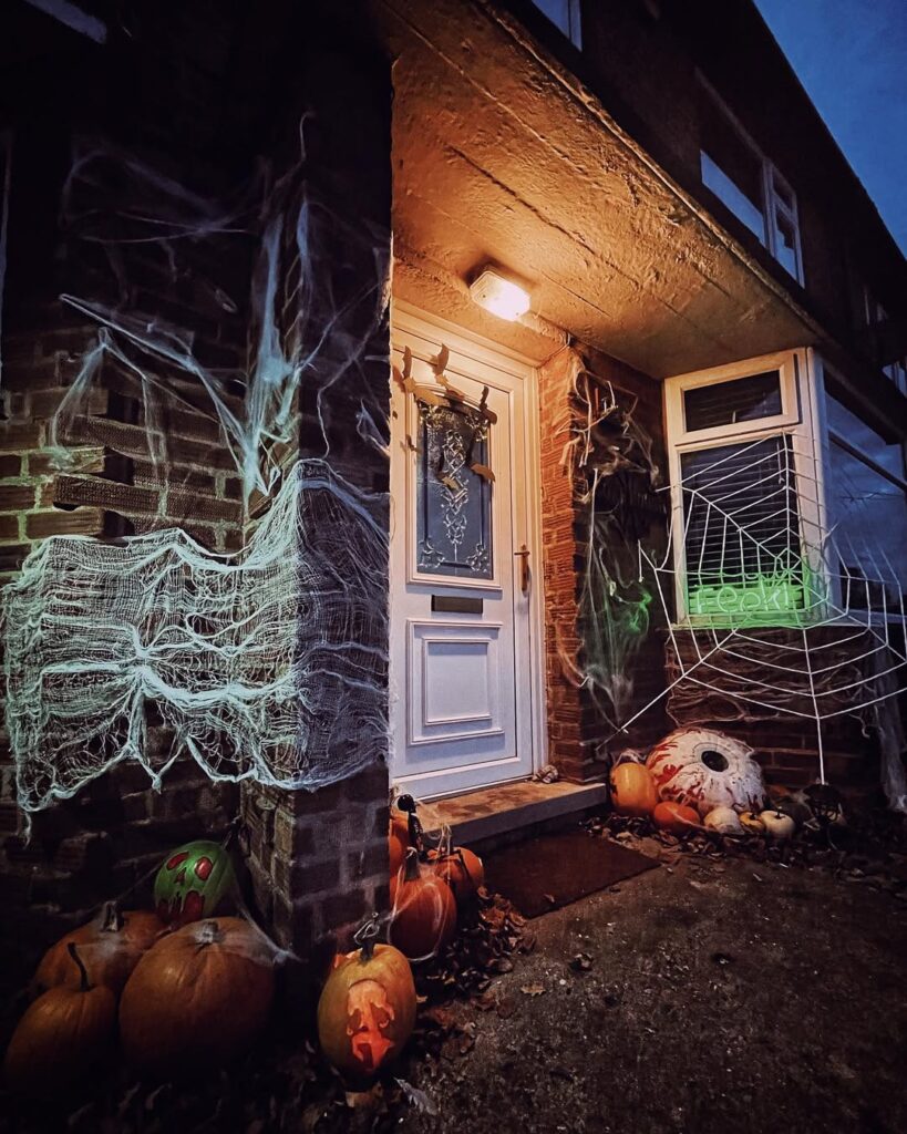 Spooky front porch decorated with glowing cobwebs, pumpkins, giant eyeball prop, and neon green "EEK!" sign.