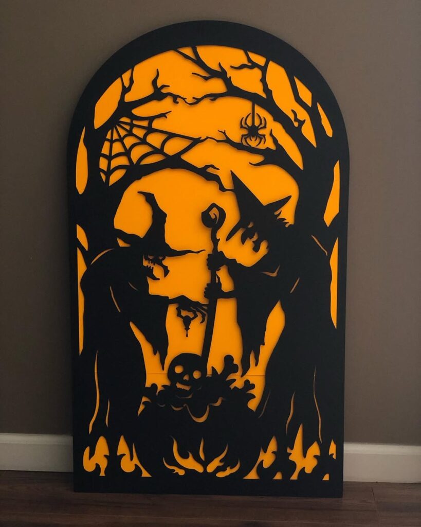 Halloween silhouette artwork of witches around a cauldron with skull, spider, trees, and glowing orange background.