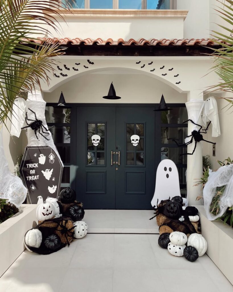 Black double doors with monochrome Halloween decor, floating witch hats, ghost cutouts, bats, pumpkins, and large spider props.