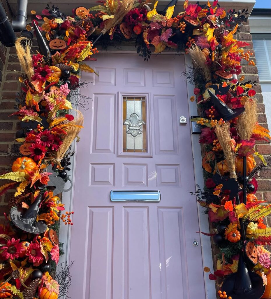 Pink front door framed with colorful fall garland of pumpkins, witch hats, orange leaves, and dried grasses.