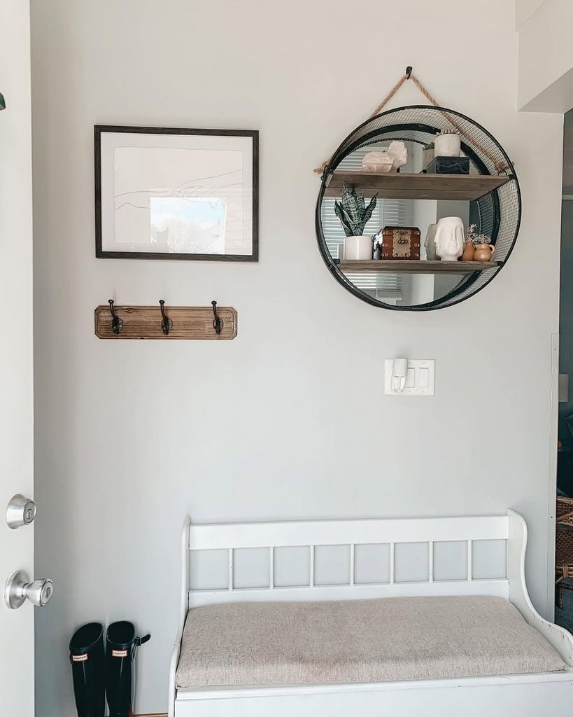 Minimalist entryway decor featuring a round mirror, floating shelf, and wall hooks in a small apartment.