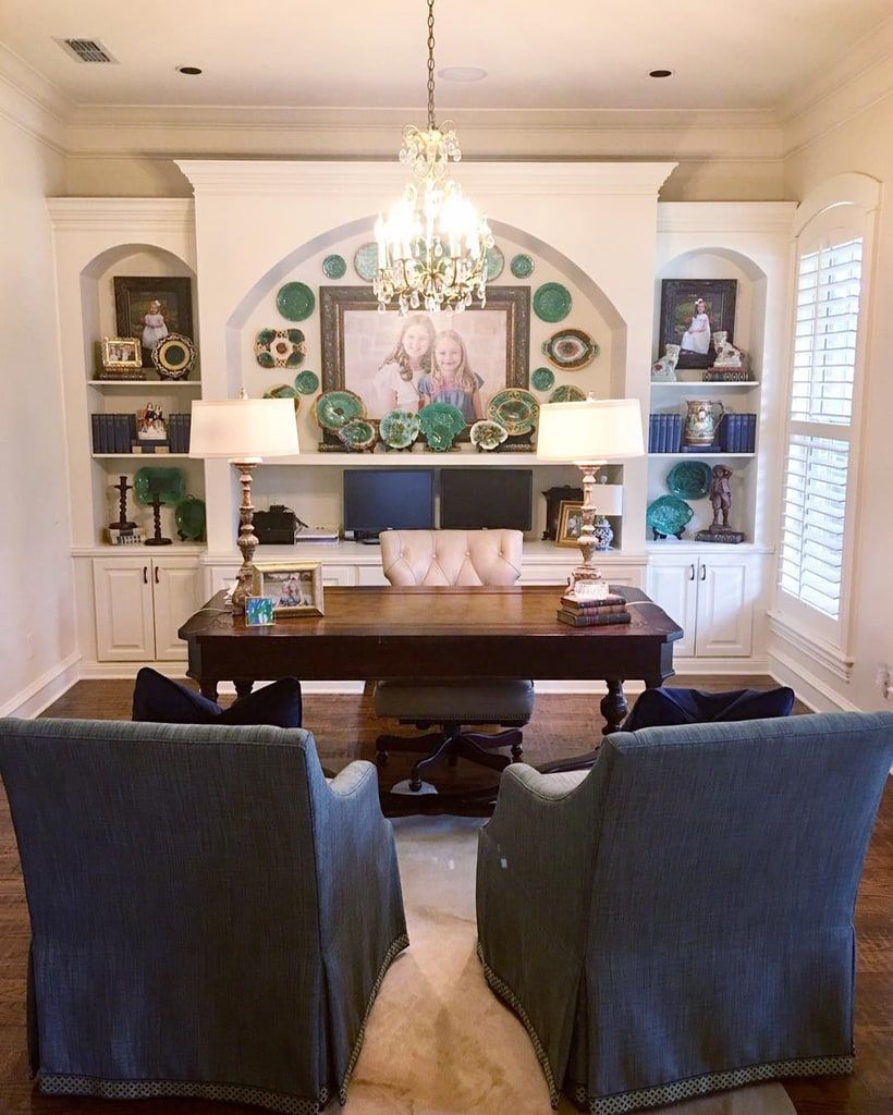 Stylish home office decor featuring a large dark wood desk, upholstered blue-green chairs, and a gallery wall of decorative plates and art.