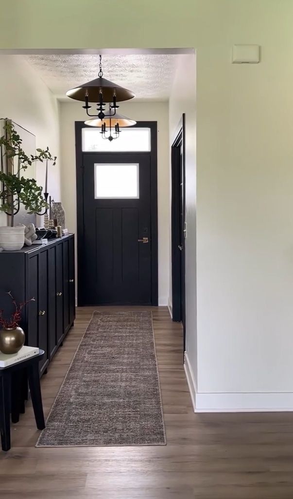 Decorated narrow entryway with dark console cabinet, neutral runner rug, and dark front door.